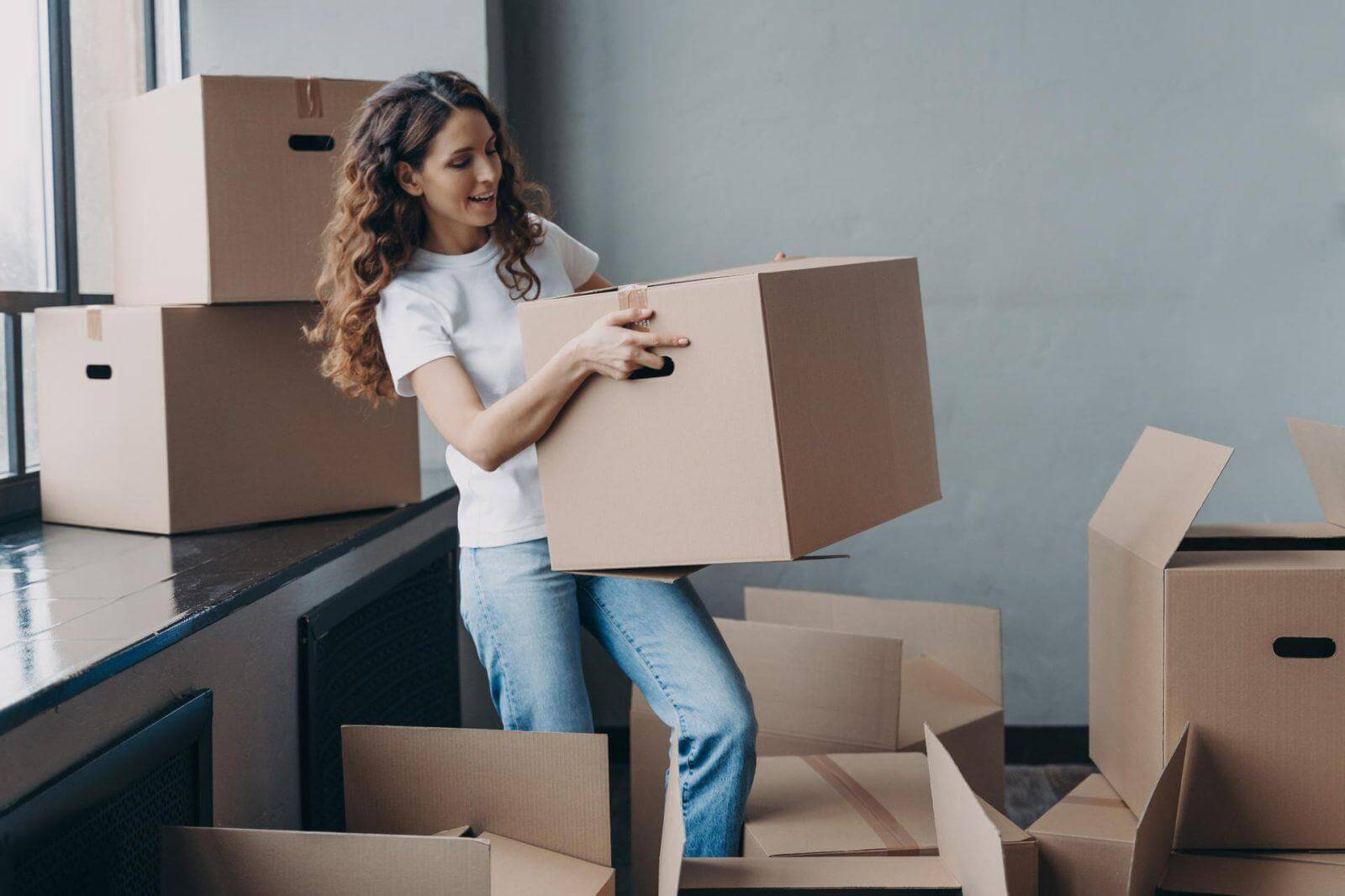 Young lady in white t-shirt is carrying cardboard box.