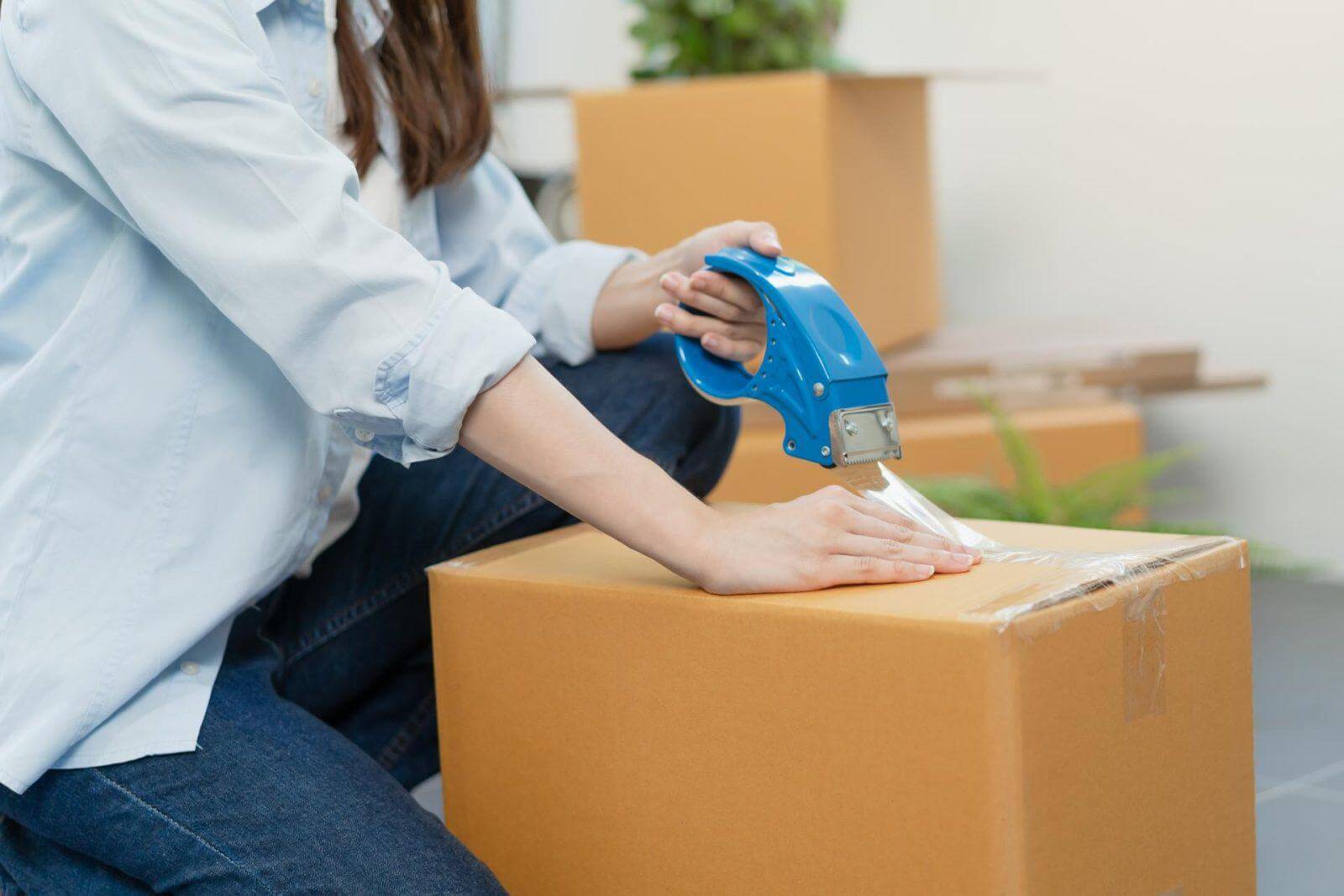 Woman using a tape gun to seal a moving box.